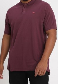 Polo shirt bordeaux en coton, avec une texture douce, un col à trois boutons et un petit logo rouge Levi's sur la poitrine.
