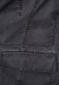 Czarny denon z gładką fakturą. Posiada widoczne szwy oraz tylną kieszeń z klapą. Ogólny, prosty design.