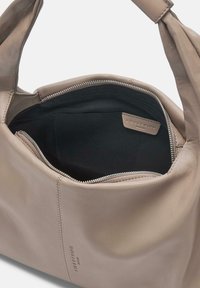 Beżowa skórzana torebka o gładkiej fakturze, zamykana na górny zamek błyskawiczny, z czarnym materiałowym wnętrzem. Posiada metkę z logo wewnątrz, bez wzoru ani akcentów.
