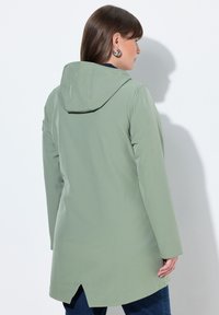 Zelená voděodolná bunda s kapucí, mírně střiženým střihem, dlouhými rukávy a rozparkem na zádech pro pohodlný pohyb.
