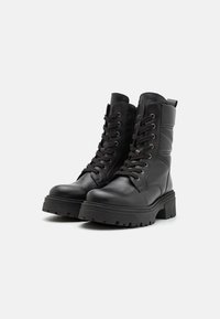 Botas de tornozelo em couro preto com biqueira redonda, design de atacadores, colarinho acolchoado e solas de borracha grossa. Apresentam detalhes em costura e alça de puxar.