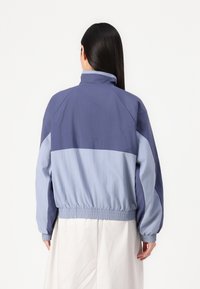 Blue and light blue jacket with a high collar, elasticized cuffs and waistband, features a two-tone design and smooth texture.