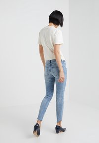 Camiseta blanca de manga corta, jeans ajustados de un azul claro y zapatos de tacón negros. El conjunto presenta una textura de denim con un lavado azul desvanecido.