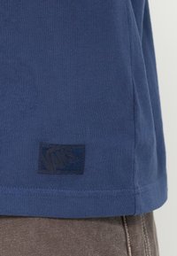 Μπλε σκούρο βαμβακερό t-shirt με υφασμένη μαύρη ετικέτα λογότυπου Vans κοντά στο τελείωμα, με απλές, καθαρές ραφές και κλασικό στρογγυλό λαιμόκοψη.