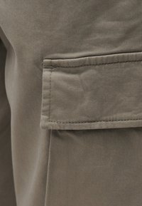 Κοντινό πλάνο τσέπης από χακί ύφασμα με πτερύγιο και ορατό ράψιμο σε ένα ένδυμα.