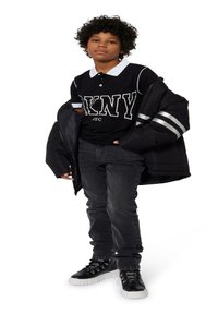 Doudoune noire avec des rayures argentées, polo noir avec col blanc et logo, jeans foncés, et baskets montantes noires avec semelles blanches.