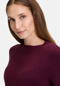 Pull en tricot bourgogne avec un col rond et un tissu doux et texturé. Le design présente une coupe décontractée et une finition lisse.