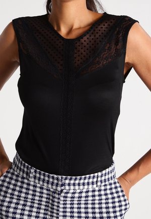 Zwart mouwloos topje met kant en een stippenmesh paneel, gecombineerd met een high-waisted zwart-witte geruite broek.