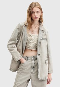 Blazer in denim grigio chiaro con vestibilità rilassata, chiusura a un bottone e taschino sul lato sinistro, abbinato a un top cropped strutturato e pantaloni coordinati.