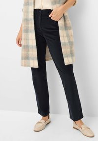 Zwarte slim-fit broeken met een rechte pijp, gecombineerd met een beige en geruit jasje en lichte loafers.