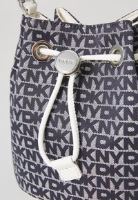 Bucketveske laget av marineblått mønstret stoff med logoen "DKNY" i vekslende hvitt og grått, med hvit snor og sølvfarget maskinvare.