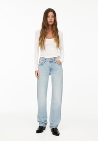 Lättviktig vit långärmad topp ihop med ljusblå vida jeanstyp, som visar en mjuk denimtextur och klassisk femficksdesign.