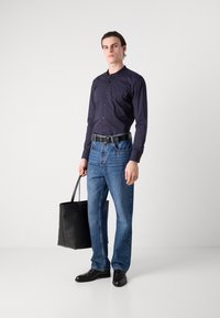 Navy button-up shirt, blue jeans, black belt, and shoes. Carries a black tote bag. Simple design and tailored fit. Smooth texture.