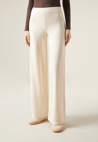 Pantalon large en tissu crème, avec une texture lisse et une taille ajustée, associé à des chaussures beige clair.
