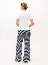 Top bianco a maniche corte abbinato a pantaloni a gamba larga blu navy e bianchi a righe. Il tessuto sembra morbido con una vestibilità comoda e senza motivi visibili.