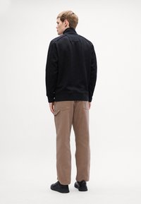 Felpa nera con texture e colletto alto, abbinata a pantaloni larghi marroni e sneakers nere. Cuciture decorative sulle spalle e sulla schiena.