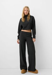 Mørkegrå, strikket, cropped sweatshirt med lange ærmer, parret med vide, højtsiddende bukser, suppleret med brune platform-sko.
