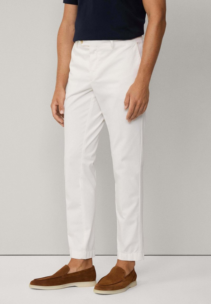 Hvide, slim-fit bukser i bomuld med en glat tekstur, med sidelommer og en tapered ankel. Kombinationen er med brune slip-on sko.