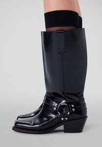 Bottes hautes en cuir noir avec une finition brillante, bout pointu, sangle décorative avec boucle et accents argentés, dotées d'un talon bloc.