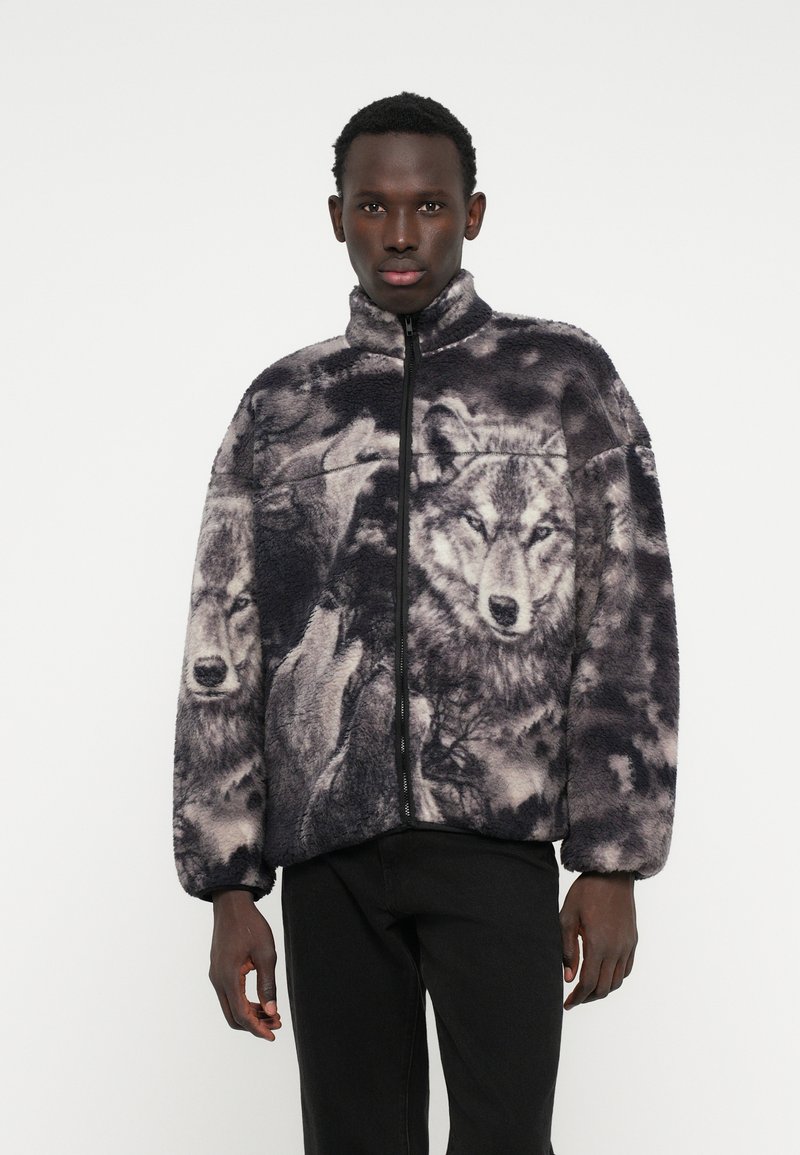 Polarowa kurtka z nadrukiem wilka w odcieniach szarości. Posiada wysoki kołnierz oraz zamek błyskawiczny z przodu, a także luźny krój.