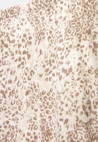 Tissu léger avec un motif léopard beige et marron, au toucher doux et à la conception fluide. Détails de couture visibles.