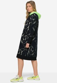 Robe hoodie noire oversize avec un motif abstrait gris, capuche verte et poignets côtelés. Assortie à des baskets accentuées de néon.