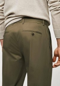Pantaloni verde oliva con vestibilità sartoriale, caratterizzati da due tasche posteriori con chiusura a bottone e passanti per cintura, realizzati in tessuto liscio.