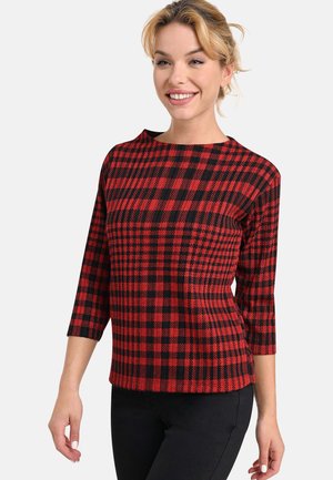 Red and black checkered top made of textured fabric, featuring three-quarter sleeves and a boat neckline, paired with black trousers.