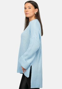 Maglione azzurro chiaro lavorato a maglia con maniche lunghe, texture a coste, spacchi laterali e vestibilità morbida. Abbinato a leggings neri per creare contrasto.
