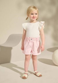 Haut blanc à côtes avec des manches volantées, associé à un short rayé rose clair avec une taille élastique. Des sandales beiges complètent la tenue.