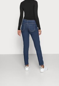 Schlanke Jeans aus dunkelblauem Denim mit einem klassischen Fünf-Taschen-Design und kontrastierenden Nähten, kombiniert mit weißen Sneakers.