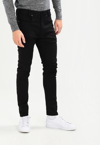 Mustat slim-fit farkut, joissa on etutaskut ja vetoketju. Yhdistetty valkoisten urheilukenkien ja harmaan neuleen kanssa.