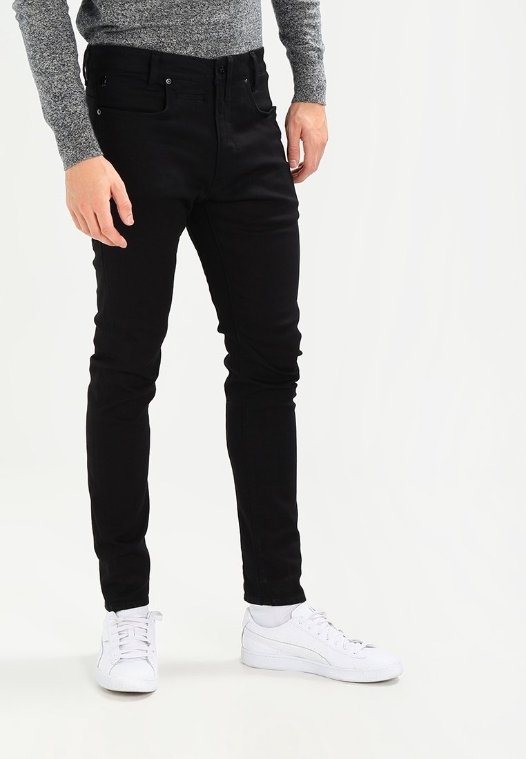 Mustat slim-fit farkut, joissa on etutaskut ja vetoketju. Yhdistetty valkoisten urheilukenkien ja harmaan neuleen kanssa.