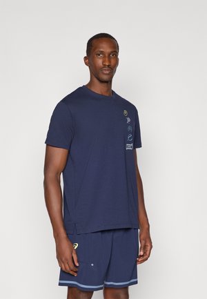 Námornícky modré bavlnené tričko s okrúhlym výstrihom, krátkymi rukávmi a dekoratívnymi farebnými vzormi na ľavej strane. Nosí sa s rovnakými šortkami.