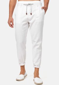 Weißes Leinenhose mit einem Kordelzugbund, gekrempelten Säumen und zwei Seitentaschen. Dazu passen weiße Slipper-ESPADRILLES.