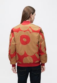 Kurtka bomberska w brązowym kolorze z dużymi czerwonymi kwiatowymi wzorami, ściągaczami na mankietach i kołnierzu. Gładka tekstura i lekko wyściełany krój.