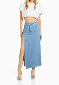 Ljusblå denim maxikjol med hög sidovenska, knapp- och dragkedjestängning samt en figurnära midjereså. Kombinerad med en vit croppad topp.