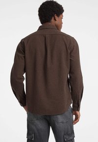 Camicia a maniche lunghe a scacchi marrone con colletto, polsini abbottonati e vestibilità rilassata, abbinata a pantaloni cargo grigi.