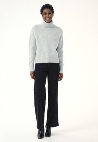 Helehall turtleneck-sviiter ribadeservade ja -äärtega, kombineeritud kõrge vöökohaga mustade laiadest pükstest ja mustadest pahkluu saapadest.