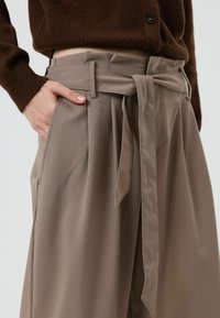 Beige wijde broek met ceintuur in de taille, plooien en zijzakken, gemaakt van zachte stof met een gladde textuur.