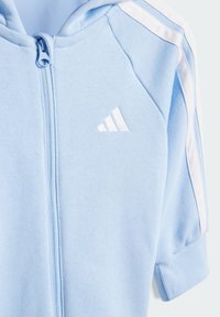 Light blue zip-up hoodie with white stripes on sleeves. Features a smooth cotton texture and an embroidered white Adidas logo.