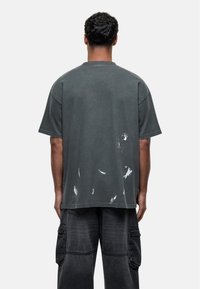 Oversized donkergrijze katoenen t-shirt met een ronde hals en verouderde witte spetters op de achterkant, met korte mouwen en een relaxte pasvorm.