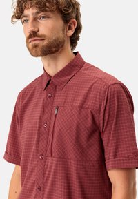 Camisa de cuadros burdeos de manga corta con cierre de botones, bolsillo en el pecho con cremallera y una textura de tela suave.