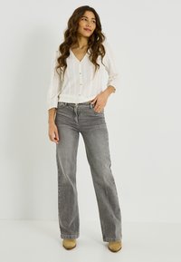 Top blanco de punto texturizado con escote en V y botones, combinado con vaqueros grises de pierna ancha y talle alto. La modelo lleva botas beige con tacón.