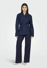 Denim jakna s preklopom, vezanjem i dugim rukavima. Uparena s širokim tamnoplaviim trapericama i svijetlim potpeticama.