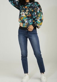 Zwart sweatshirt met bloemenpatroon en pofmouwen, gecombineerd met getailleerde blauwe spijkerbroek en witte sneakers. Stoffen met een gladde afwerking en elastische boorden.