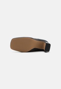 Black leather shoe sole with a square shape, featuring a tan rubber bottom and textured grip for traction. Clean design with minimal detailing.