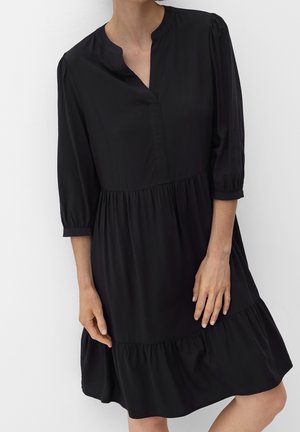 Czarna sukienka z okrągłym dekoltem w kształcie litery V, rękawami do ćwiartki oraz stopniowanym, falbaniastym dołem. Wykonana z lekkiego materiału o gładkiej fakturze.