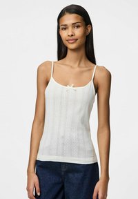 Top blanco sin mangas con tirantes finos, que presenta un patrón texturizado y un pequeño lazo en el centro. Tejido suave con una silueta ajustada.