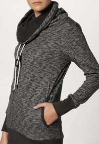 Czarna i szara melanżowa bluza z kapturem, z kołnierzem typu cowl, sznurkiem ściągającym i kieszeniami z przodu. Posiada dopasowany krój oraz kontrastowe mankiety.